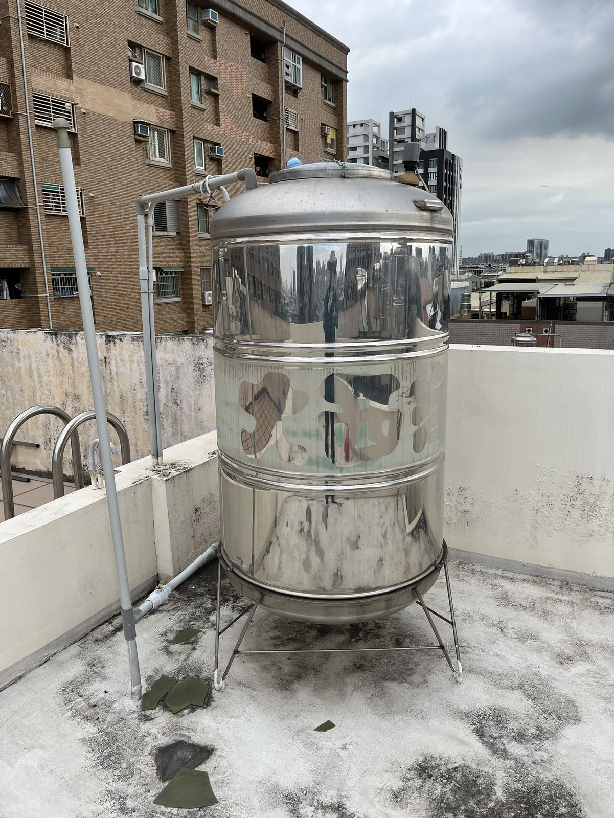 高雄鳳山區透天住宅頂樓的不鏽鋼水塔實拍,旁可見周邊老建物與屋頂環境。